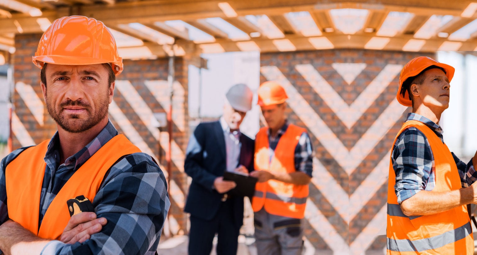 Two contractors in hard hats and safety vests on a job site, with a crew talking in the background